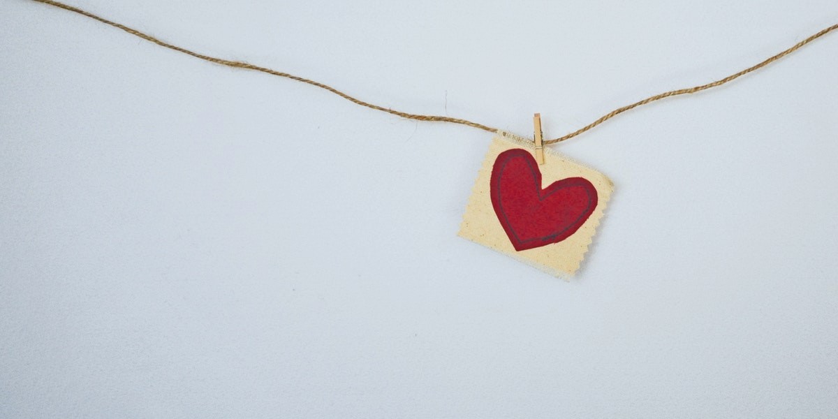 Red heart on fabric card hanging from twine with clothespin, minimalistic love concept.