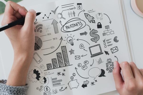 Hand drawing business strategy concepts with graphs, arrows, and icons on white paper.