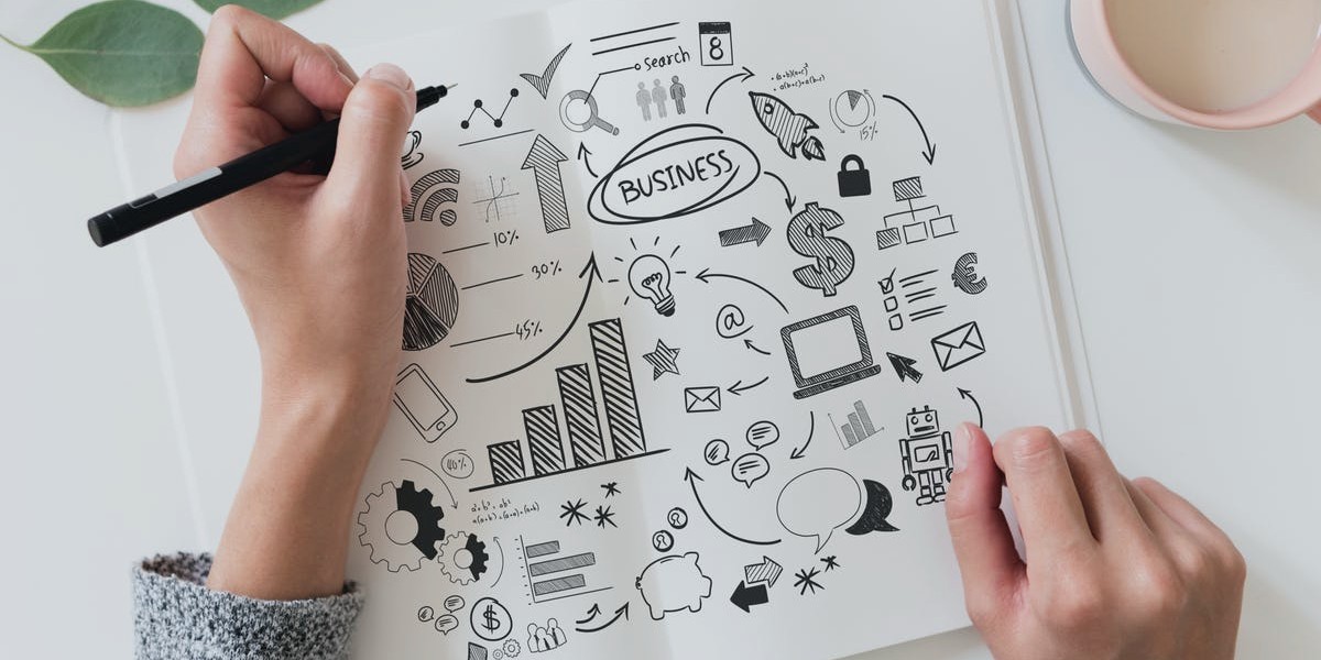 Hand drawing business strategy concepts with graphs, arrows, and icons on white paper.