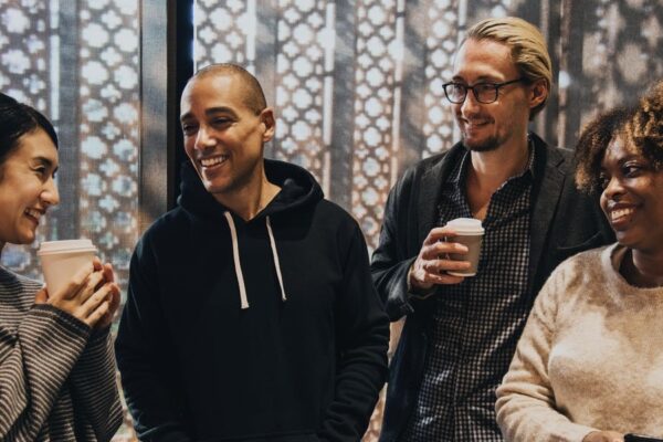 Group of diverse people sharing a laugh over coffee in a warmly lit room with a decorative background.