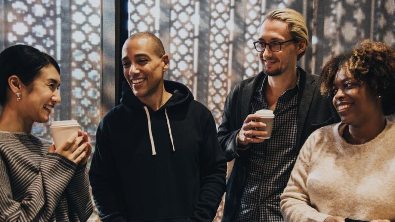 Group of diverse people sharing a laugh over coffee in a warmly lit room with a decorative background.