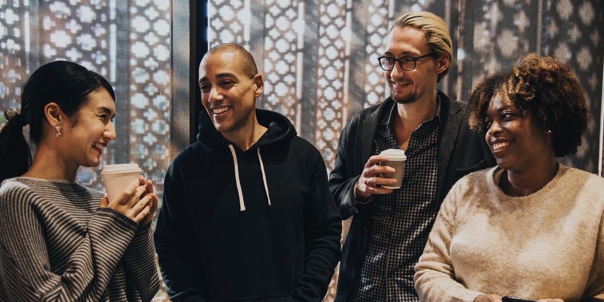 Group of diverse people sharing a laugh over coffee in a warmly lit room with a decorative background.