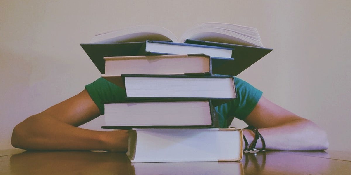 Person overwhelmed by a stack of books, highlighting a challenging study session.