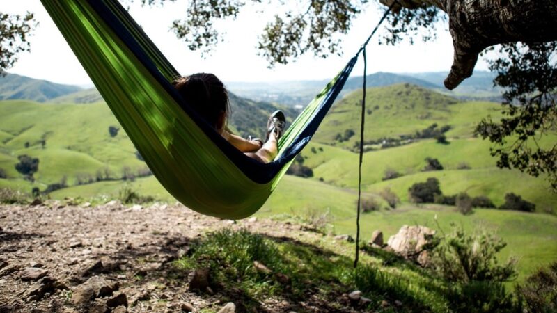 Person relaxing in a green hammock, enjoying panoramic view of rolling hills and nature.