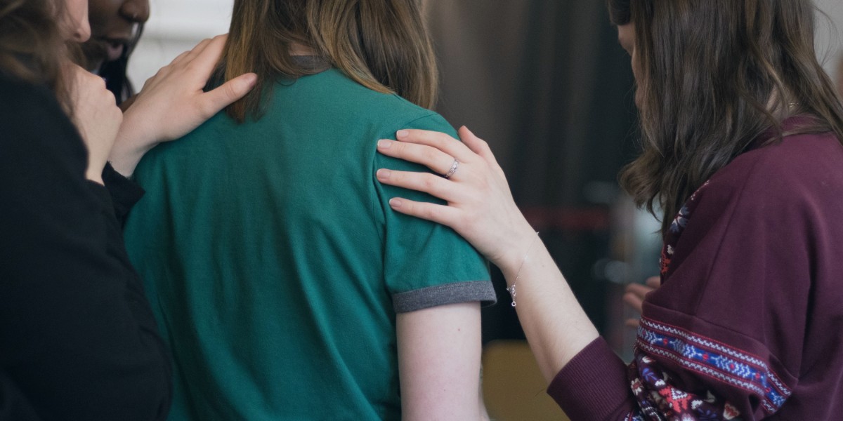 Group providing emotional support with hands on a person's shoulders.
