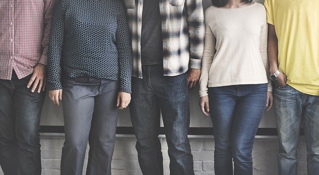 Group of five casually dressed individuals standing against a white brick wall, showcasing diverse outfits and styles.