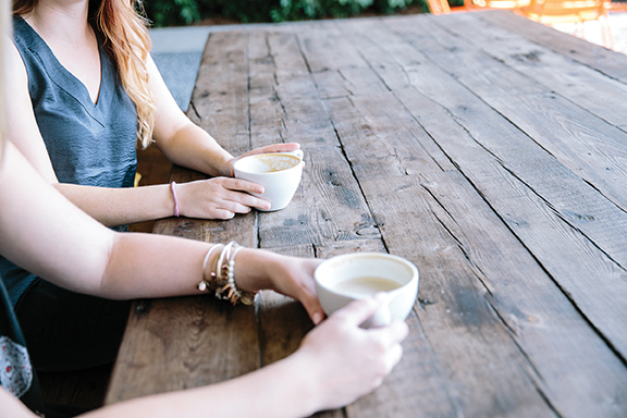 Two people enjoying coffee at a rustic wooden table outdoors.