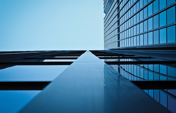 Upward view of a modern skyscraper with glass facade against a clear blue sky, capturing urban architecture and symmetry.