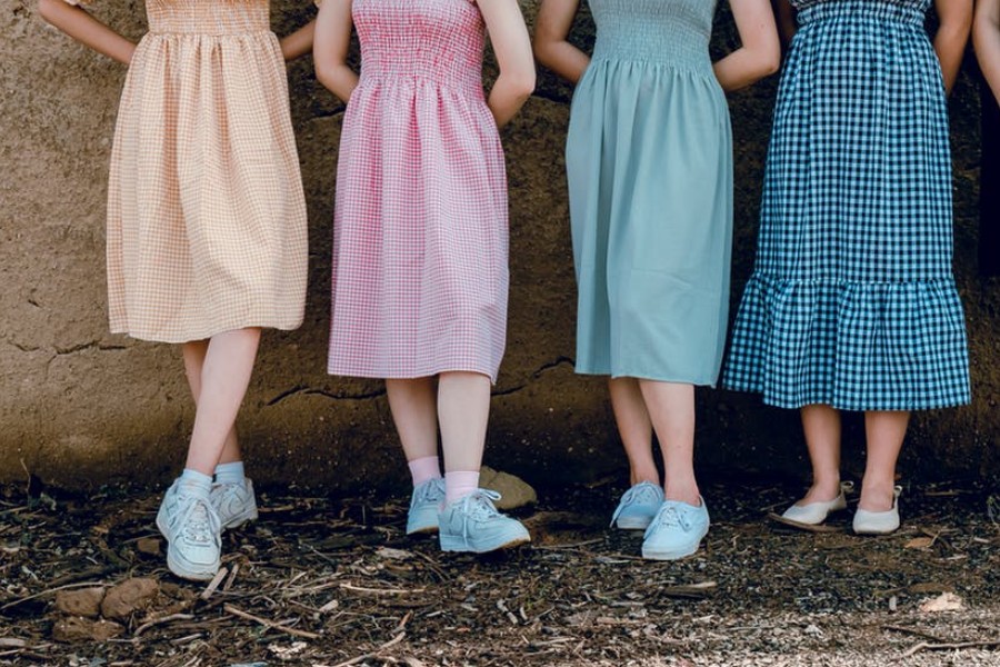 Four women in colorful gingham dresses and sneakers, standing side by side outdoors, showcasing summer fashion.