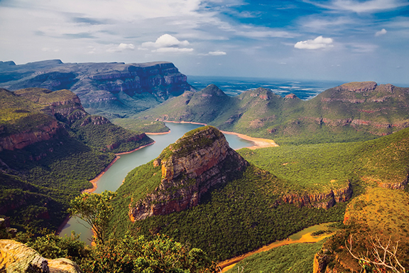 Majestic panoramic view of Blyde River Canyon with lush green landscape and winding river under a blue sky.