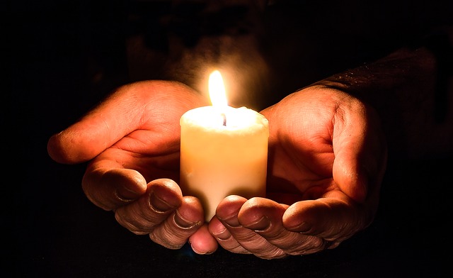 Hands gently holding a lit candle in the dark, symbolizing hope, warmth, and tranquility.
