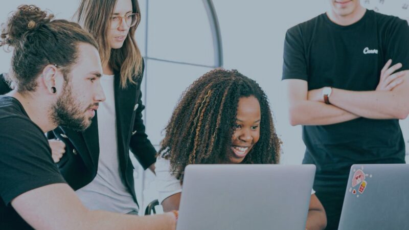 Group of diverse colleagues collaborating on laptops with smiles in a bright office space.