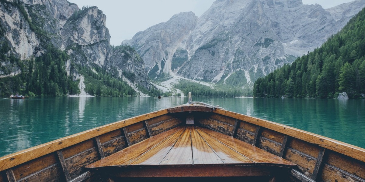Wooden boat on a serene lake surrounded by majestic mountains and lush forests. Ideal for nature and travel inspiration.