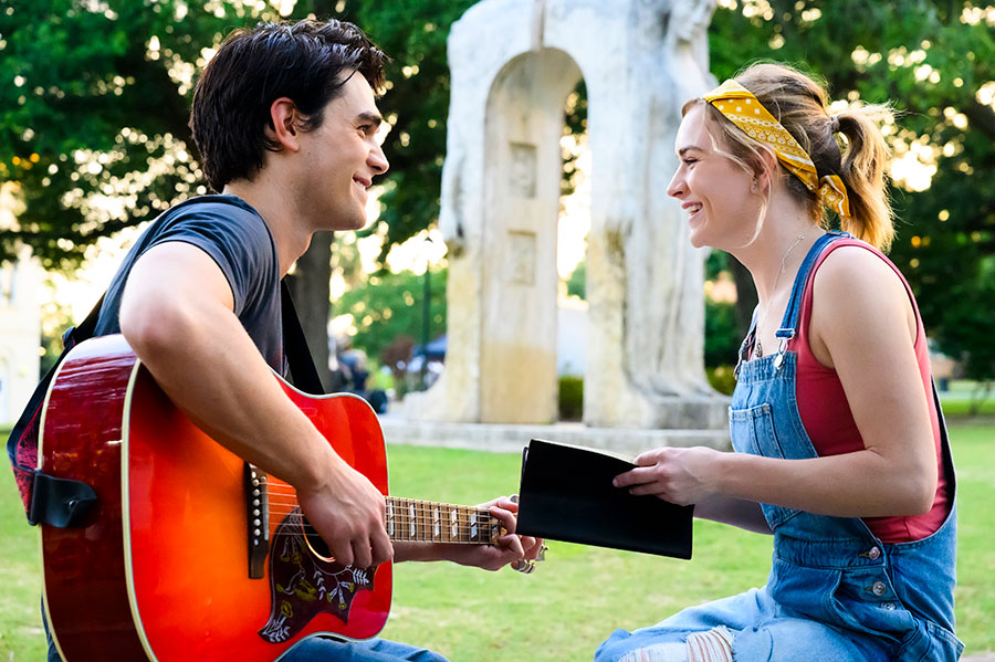 Young couple enjoying an outdoor guitar session in a park, woman holds notebook and smiles at guitarist.