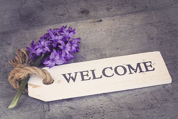 Rustic welcome sign with purple flowers on a wooden surface, evoking warmth and hospitality.