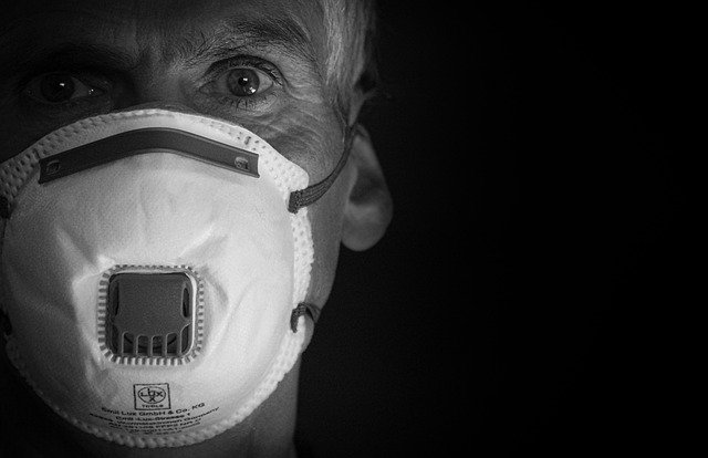 Person wearing a protective face mask with filter, set against a dark background for safety and health awareness.