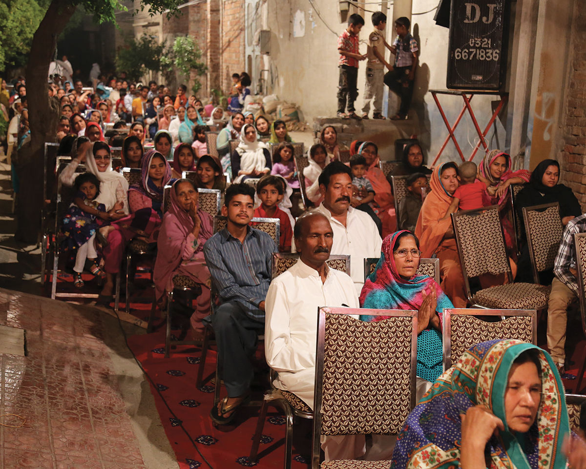 A diverse community gathering in an outdoor setting, seated attentively and engaged in an event.