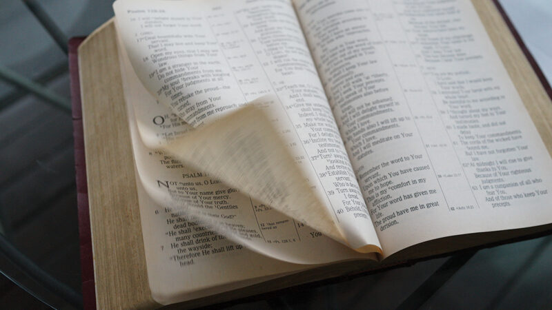 Open Bible with turning pages, showcasing Psalms text, on a glass table.