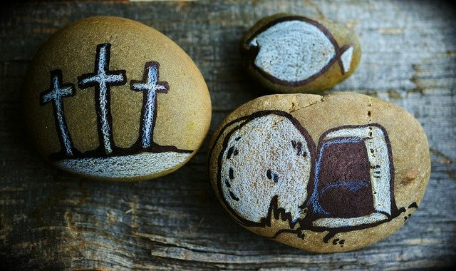 Painted stones with Christian symbols: three crosses, an angel, and a fish on a wooden surface.