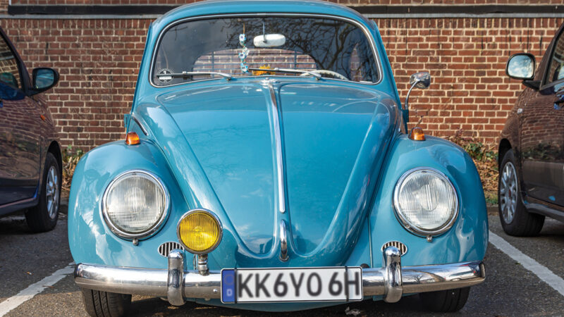 Vintage blue car parked in a lot, front view with distinctive round headlights.