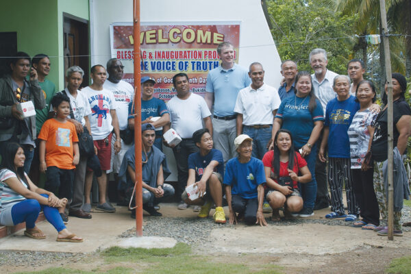 Group photo at community event with Welcome sign, outdoors, smiling people.