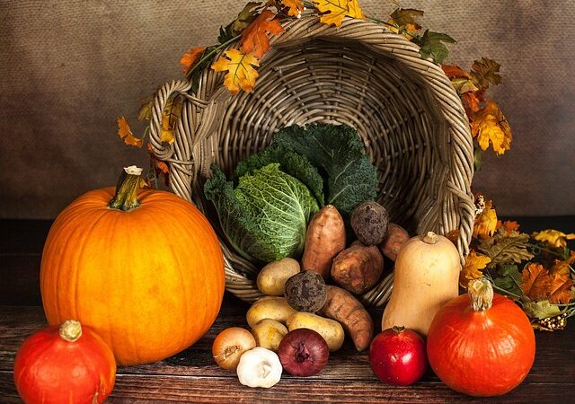 Cornucopia with pumpkins, cabbage, sweet potatoes, and fall leaves, representing an autumn harvest theme.