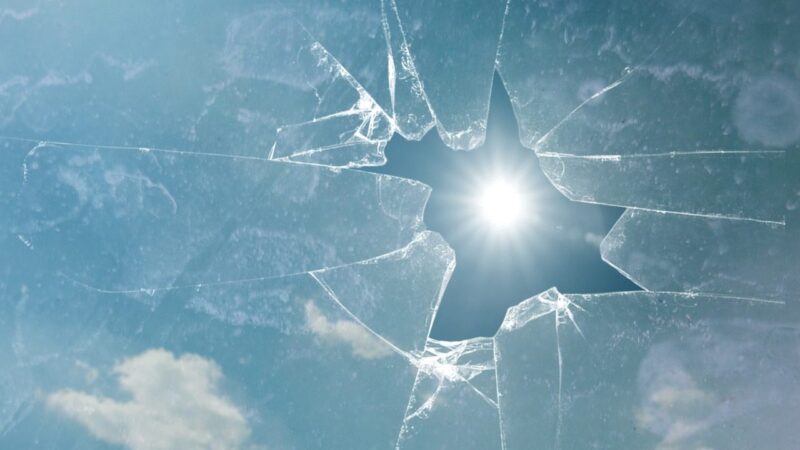 Cracked glass with sunlight shining through against a blue sky backdrop.