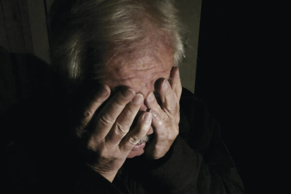 Elderly person covering face with hands in dim lighting, conveying emotion and vulnerability.