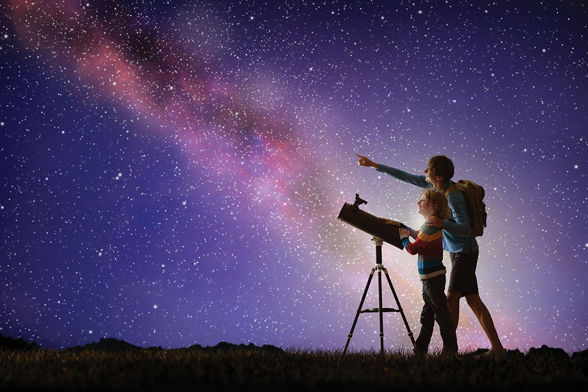 Father and child stargazing with telescope under a starry sky.