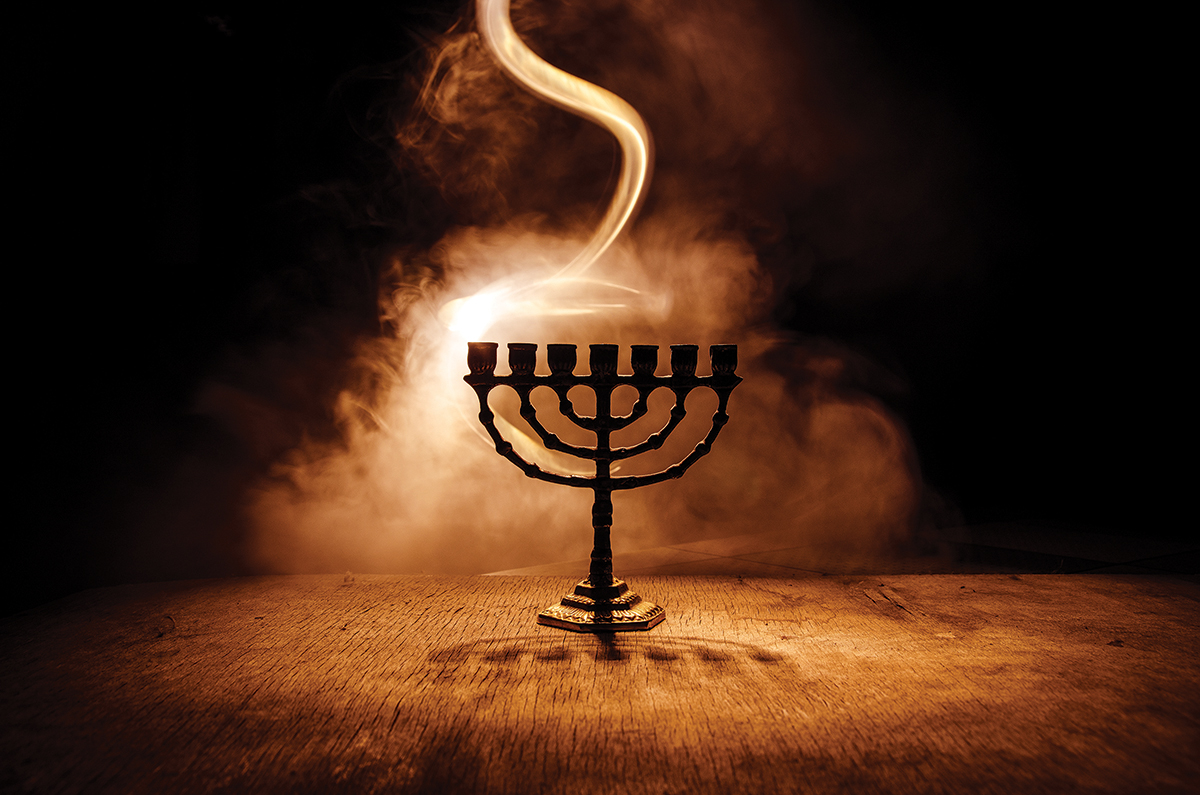 Menorah with nine branches casting shadow in smoky, dimly lit atmosphere, symbolizing a cultural celebration.