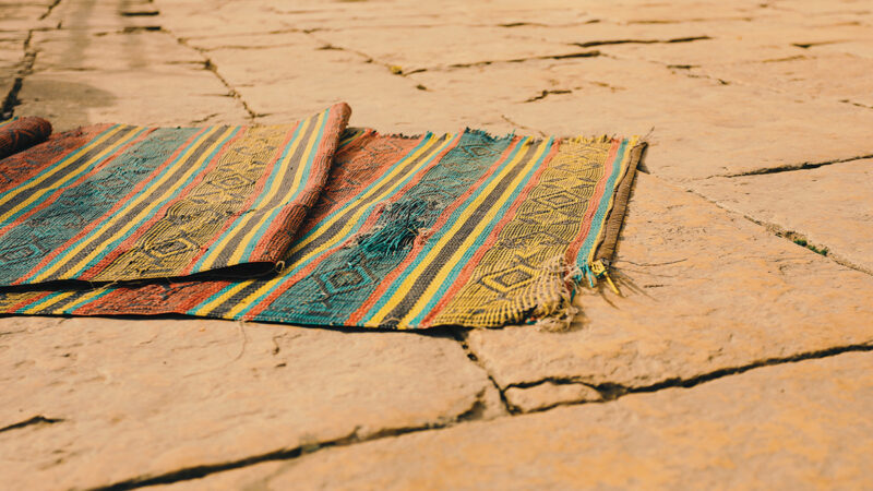 Colorful woven rug on rustic stone pathway outdoors in warm lighting.