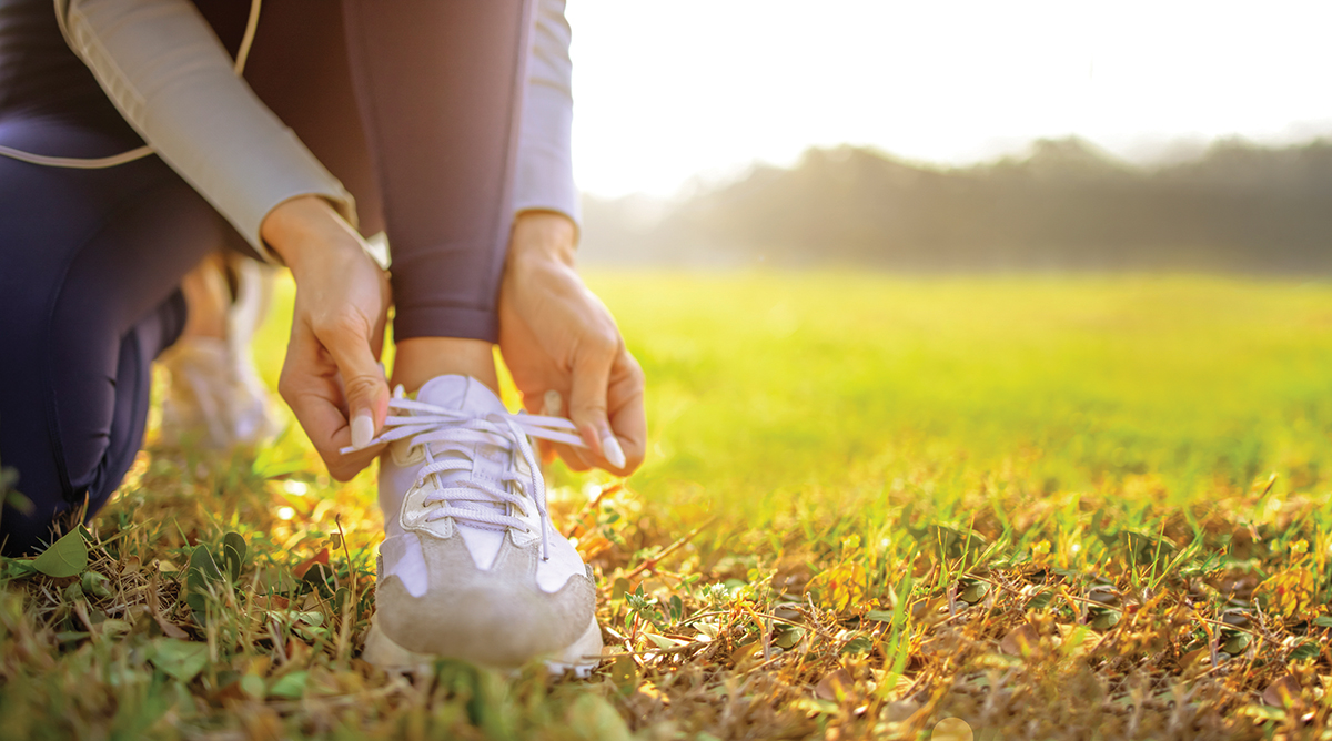 Runner tying shoelaces on a sunny day in a grassy field, preparing for an outdoor workout.