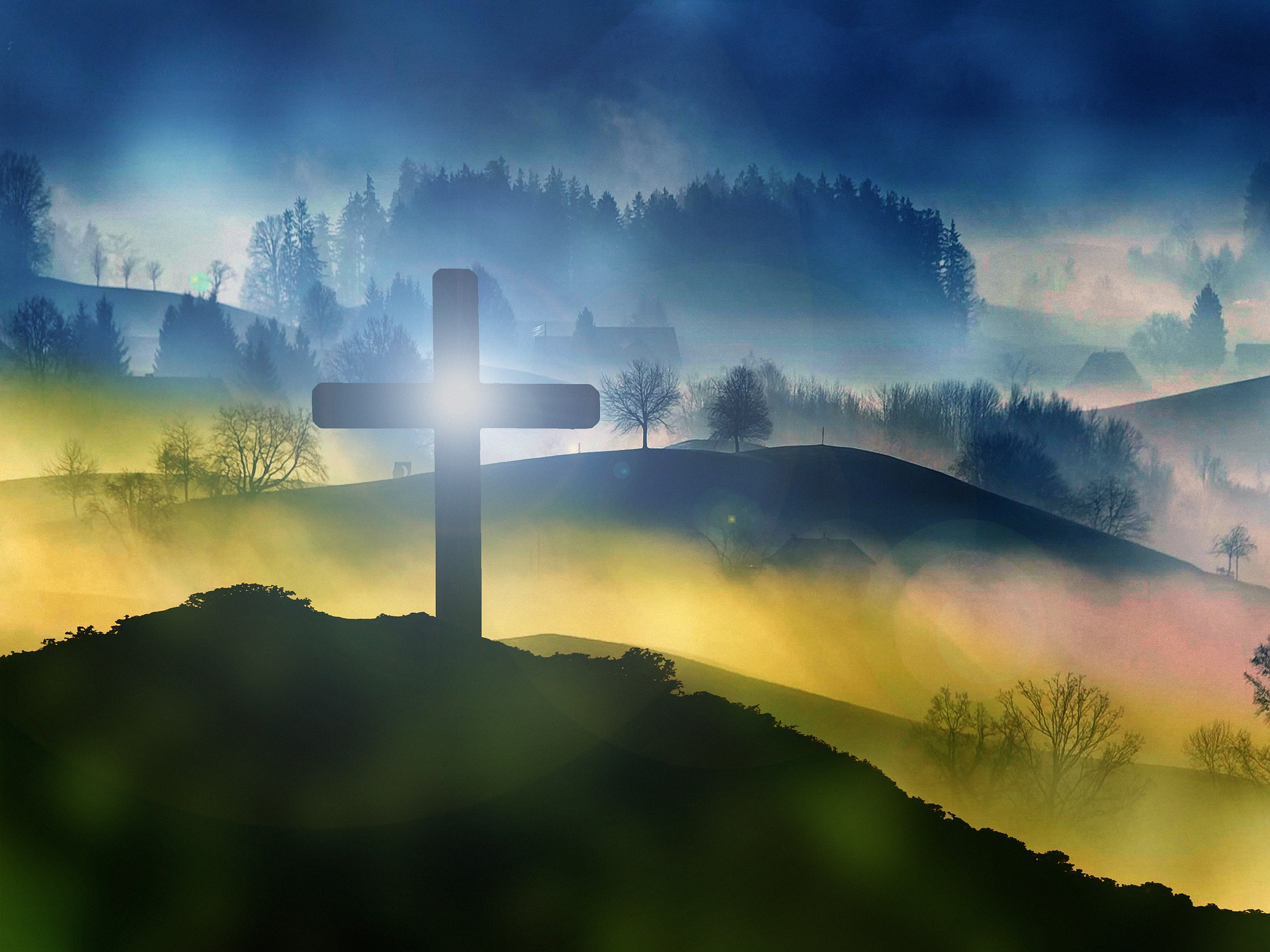 Silhouette of a cross on a misty hill with sunrise, forest, and foggy landscape in the background.