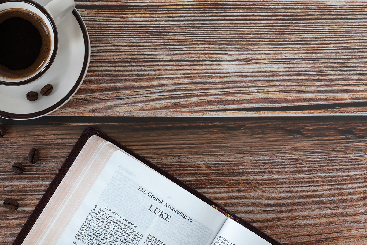 Open holy bible book Luke gospel with coffee cup on wooden background, copy space, top view