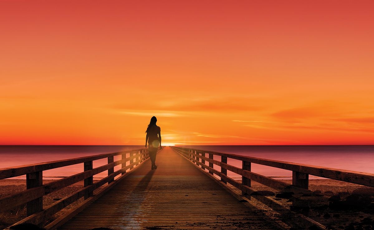 Silhouette of a woman on a jetty at sunset by the sea