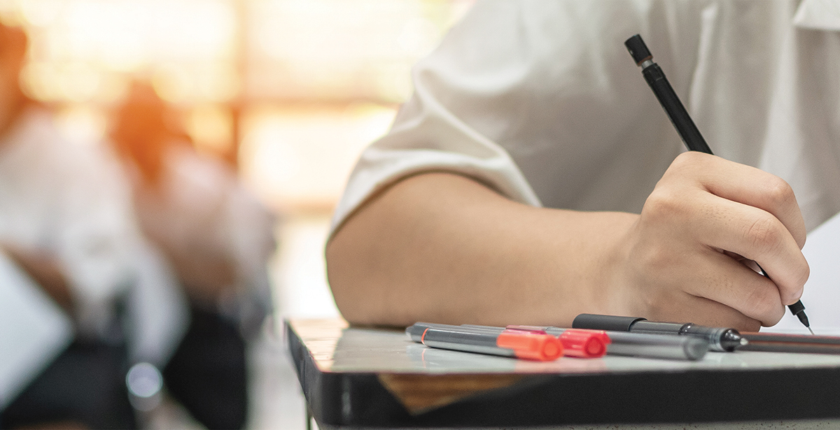 Exam at school with student's taking educational admission test in class, thinking hard, writing answer in university classroom, education and world literacy day concept